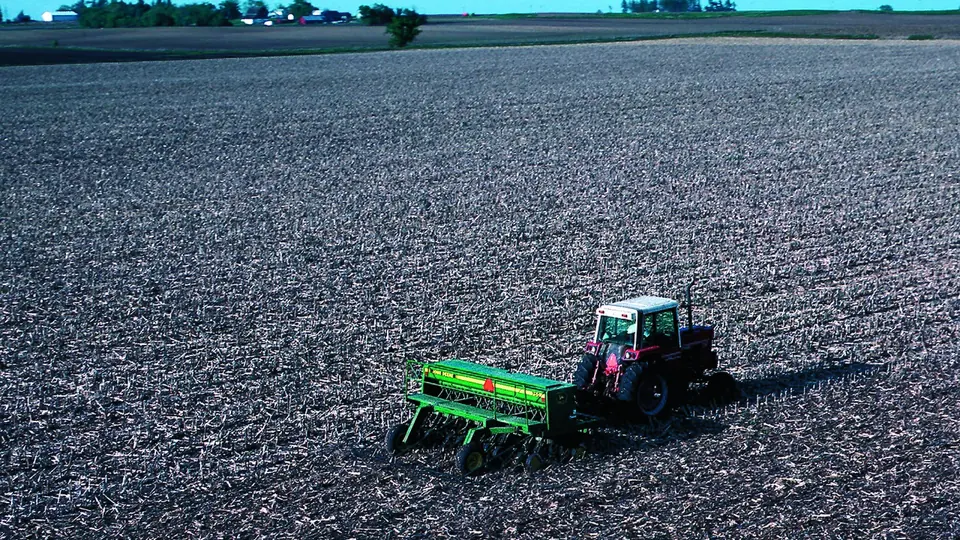 Trator com semeadora de plantio direto abrindo linhas em solo preparado