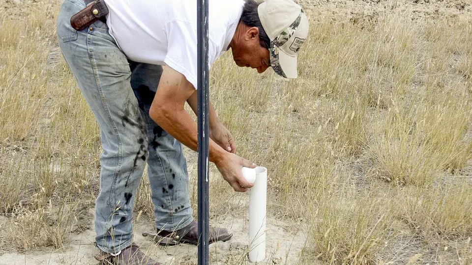 Homem coletando amostra de solo com trado em área de campo seco