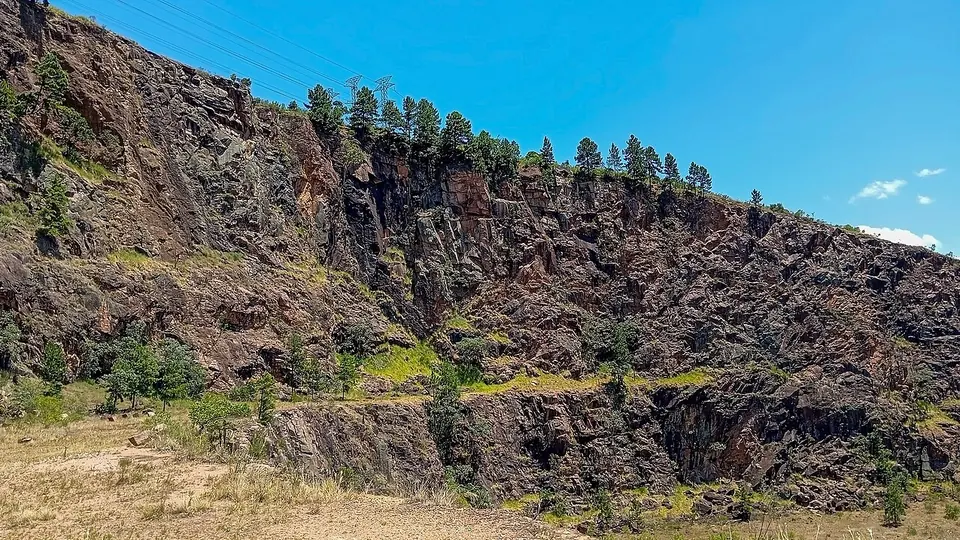 Paredão de pedreira com rocha exposta no corte e vegetação no topo