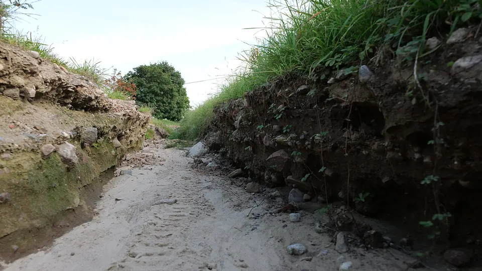 Barranco de solo nu aberto pela enxurrada, com sulco de erosão no caminho