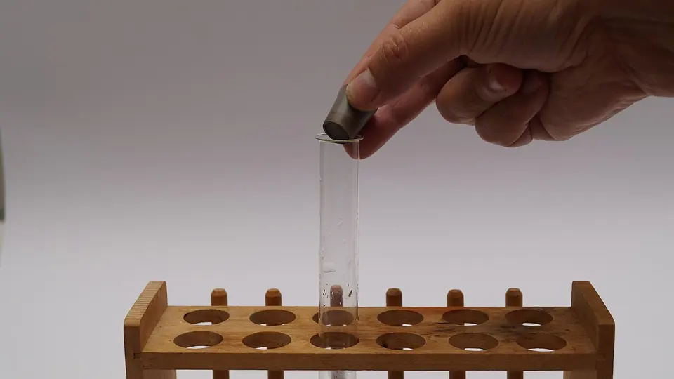 Mão colocando tubo de ensaio em suporte de madeira na bancada do laboratório