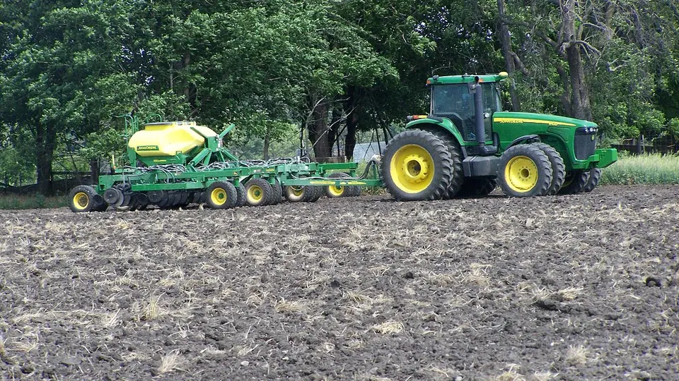 Trator com plantadeira acoplada trabalhando em lavoura recém-preparada
