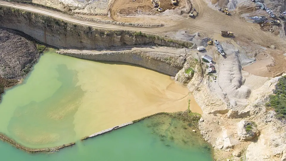 Cava de mineração a céu aberto com bancadas de rocha e lago esverdeado