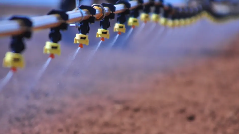 Bicos de um pivô de irrigação lançando jatos de água sobre o solo da lavoura