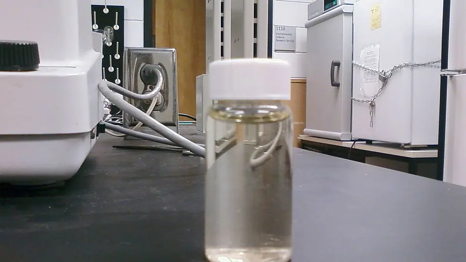 Frasco de amostra sobre a bancada de um laboratório com equipamentos ao fundo