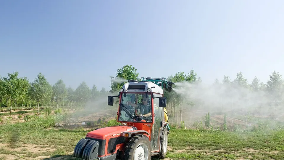 Trator pulverizador aplicando calda na lavoura em dia de sol
