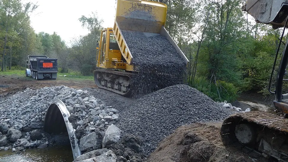 Monte de pedra moída cinza sendo despejado por máquina de esteira
