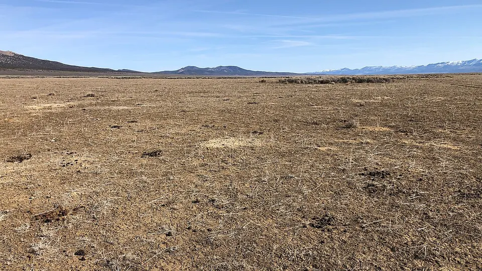 Campo de solo nu e seco se estendendo até os morros ao fundo